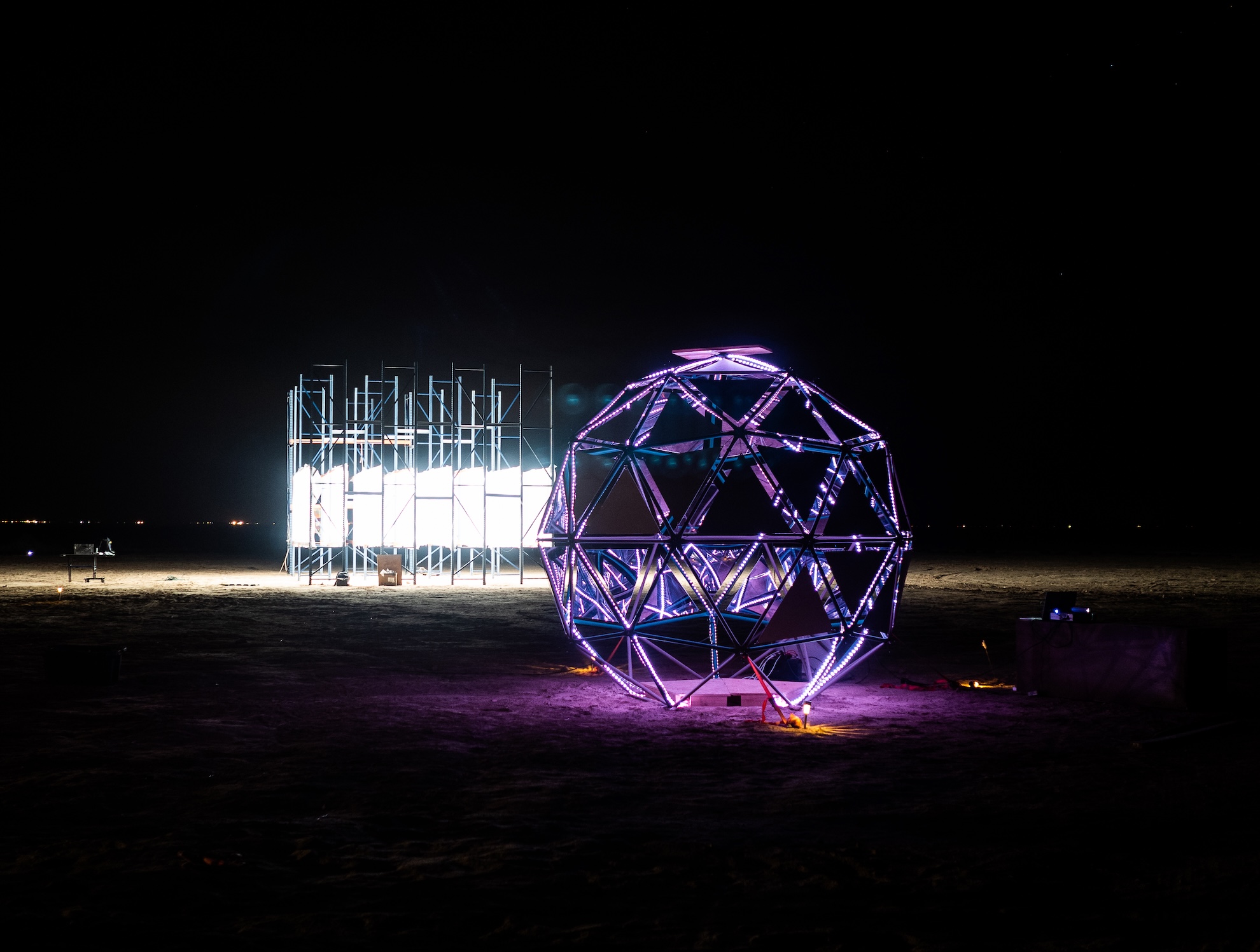A geodesic dome lit with purple lights in the desert at night.