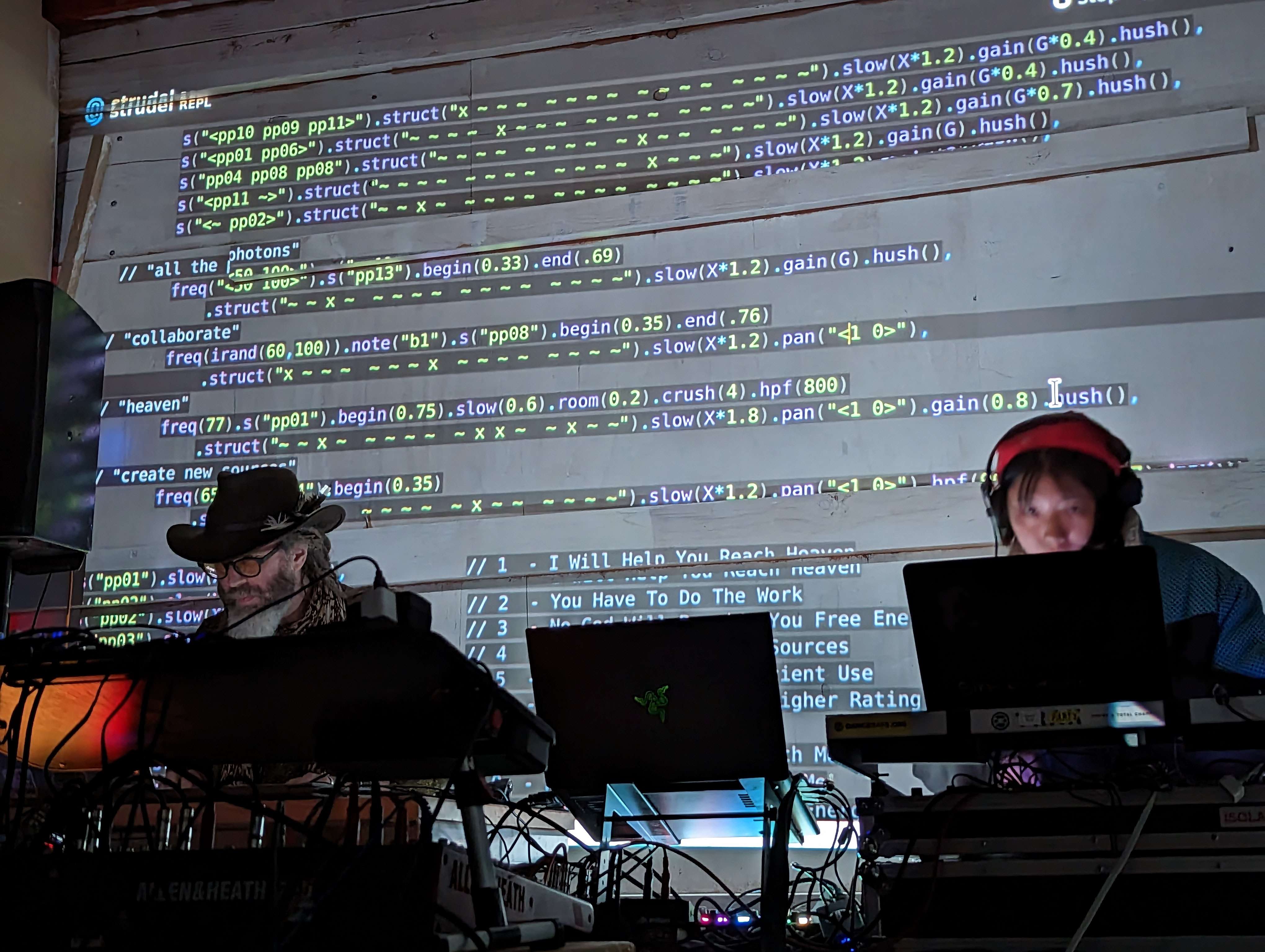 Two people live-coding music with code projected on the wall behind them.
