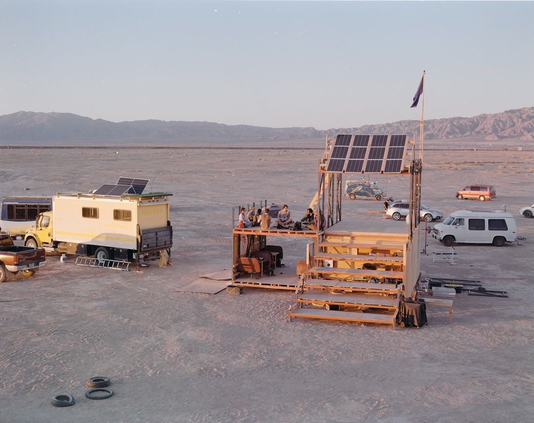 A multi-level wooden structure with solar panels, serving as a gathering spot.