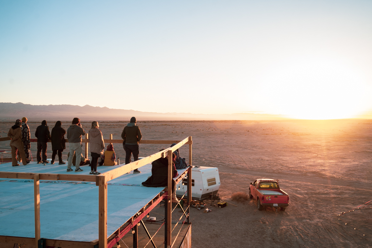 People watching the sunset from a raised platform in the desert.