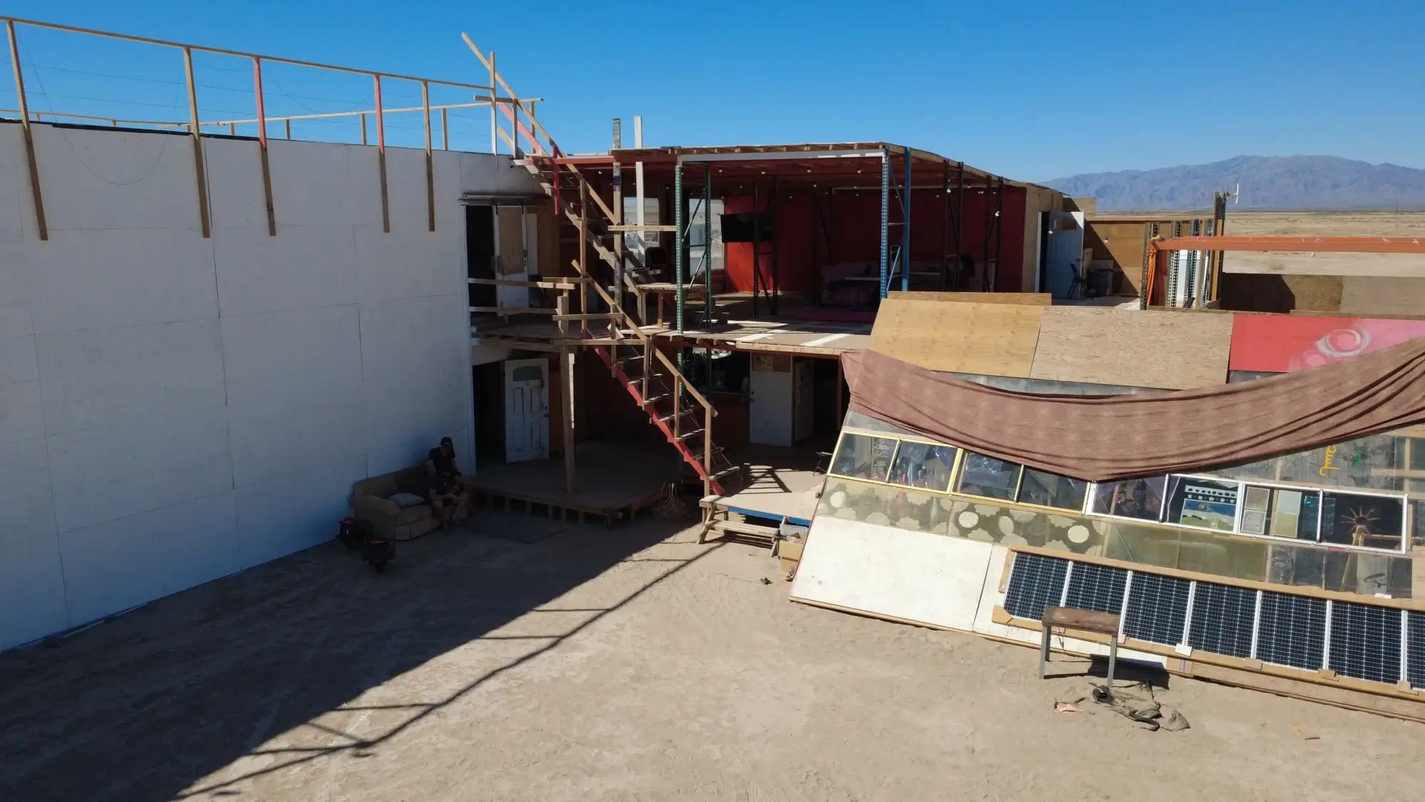 Drone view of the multi-story pallet-rack campus at Mars — plywood mezzanines, solar panels, and open desert behind