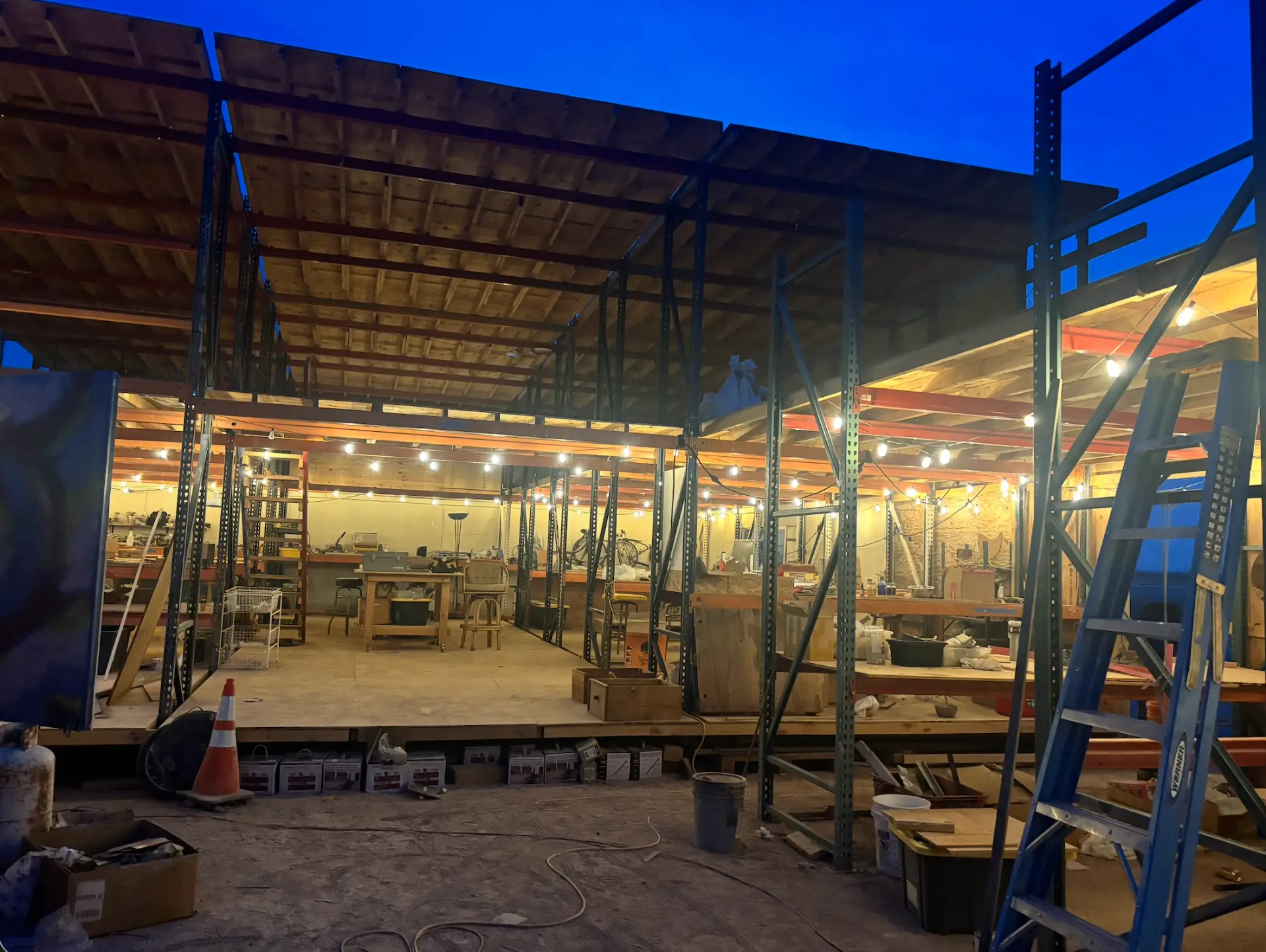 The workshop at dusk, warm string lights under a deep blue sky
