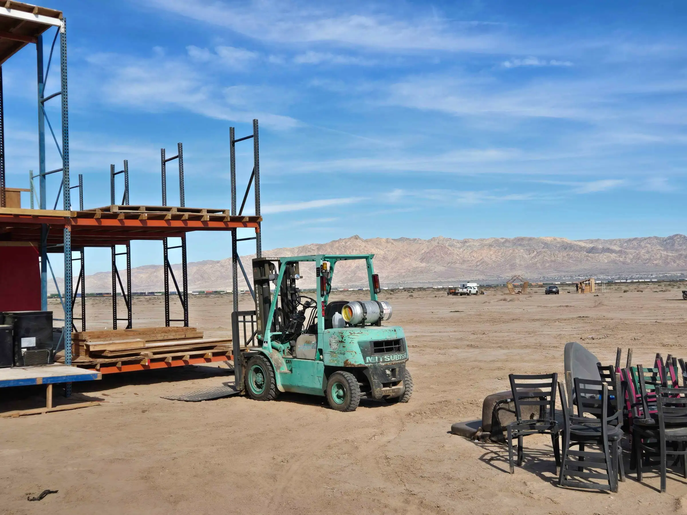 A forklift parked by a half-built pallet-rack structure on the desert lake bed during the build