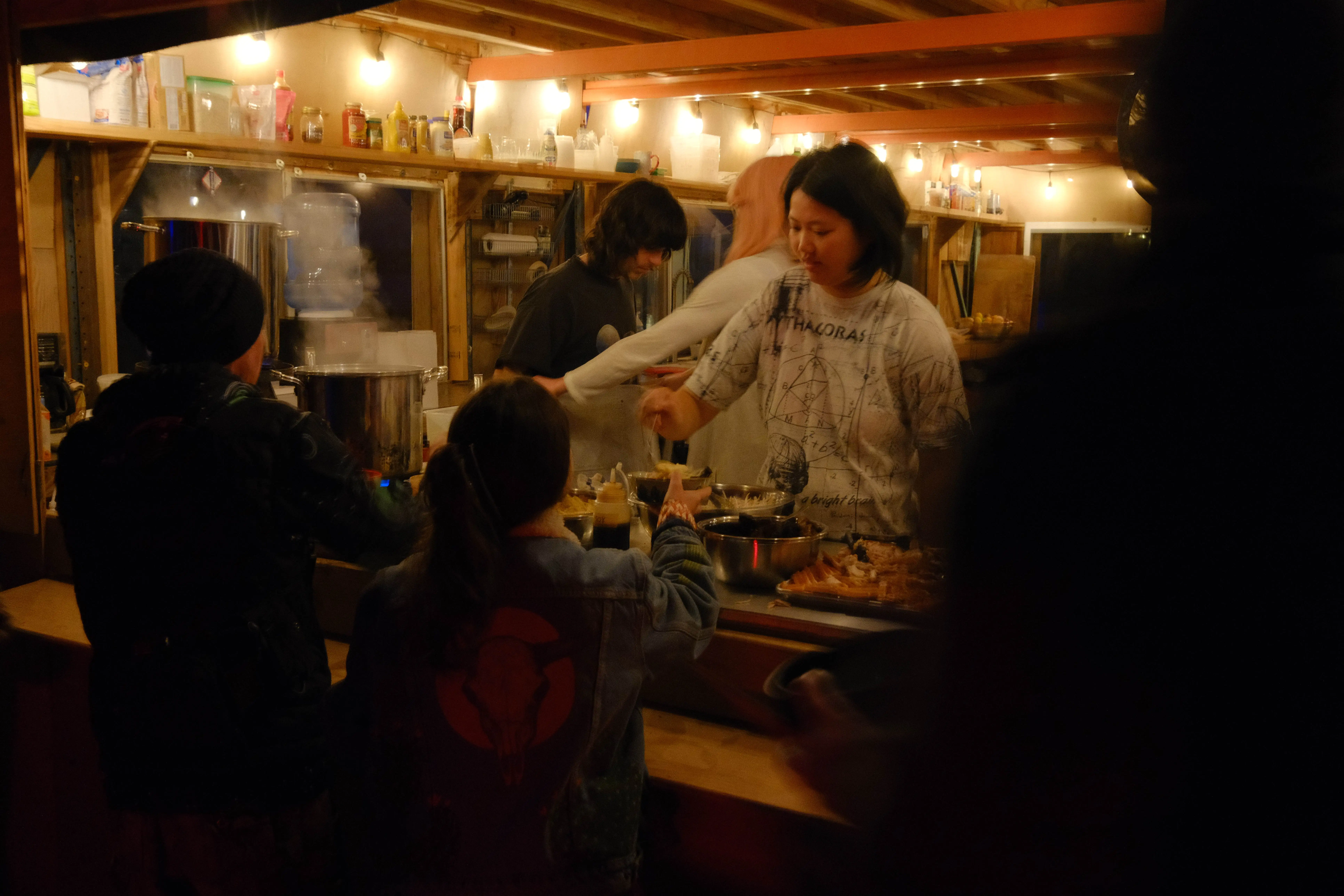 The 2026 camp kitchen at night, cooking and serving under string lights
