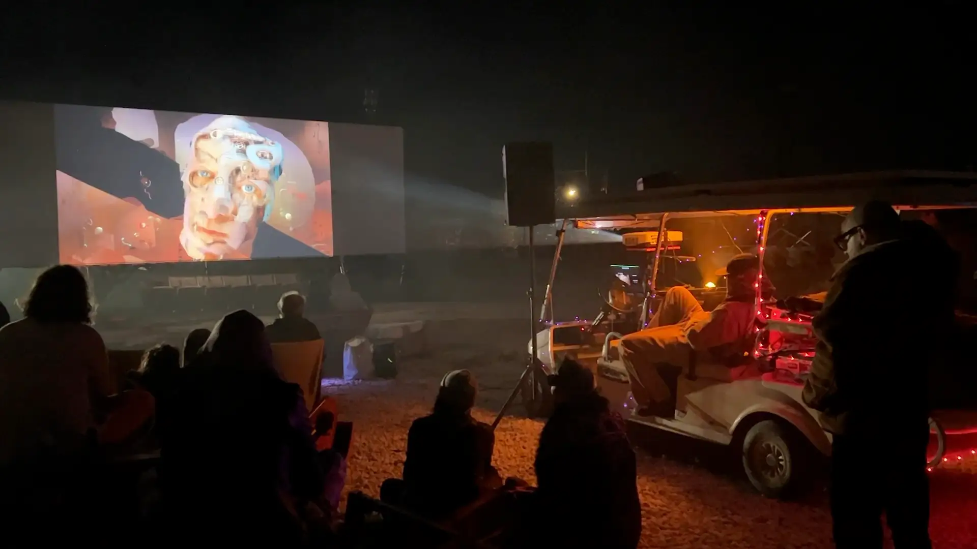 Audience silhouetted against the drive-in screen, a projector running from a fairy-lit golf cart · 2023