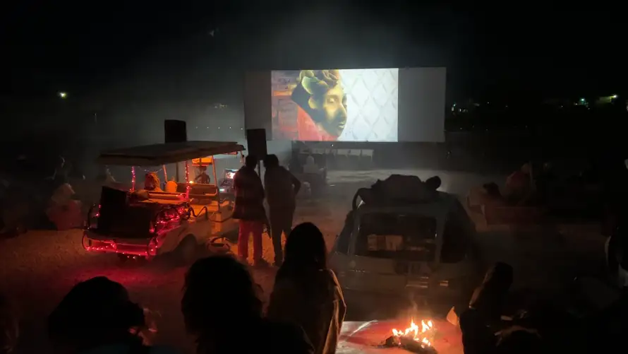 Night screening at the Bombay Beach Drive-In, a lit cart and campfire beside the audience · 2023