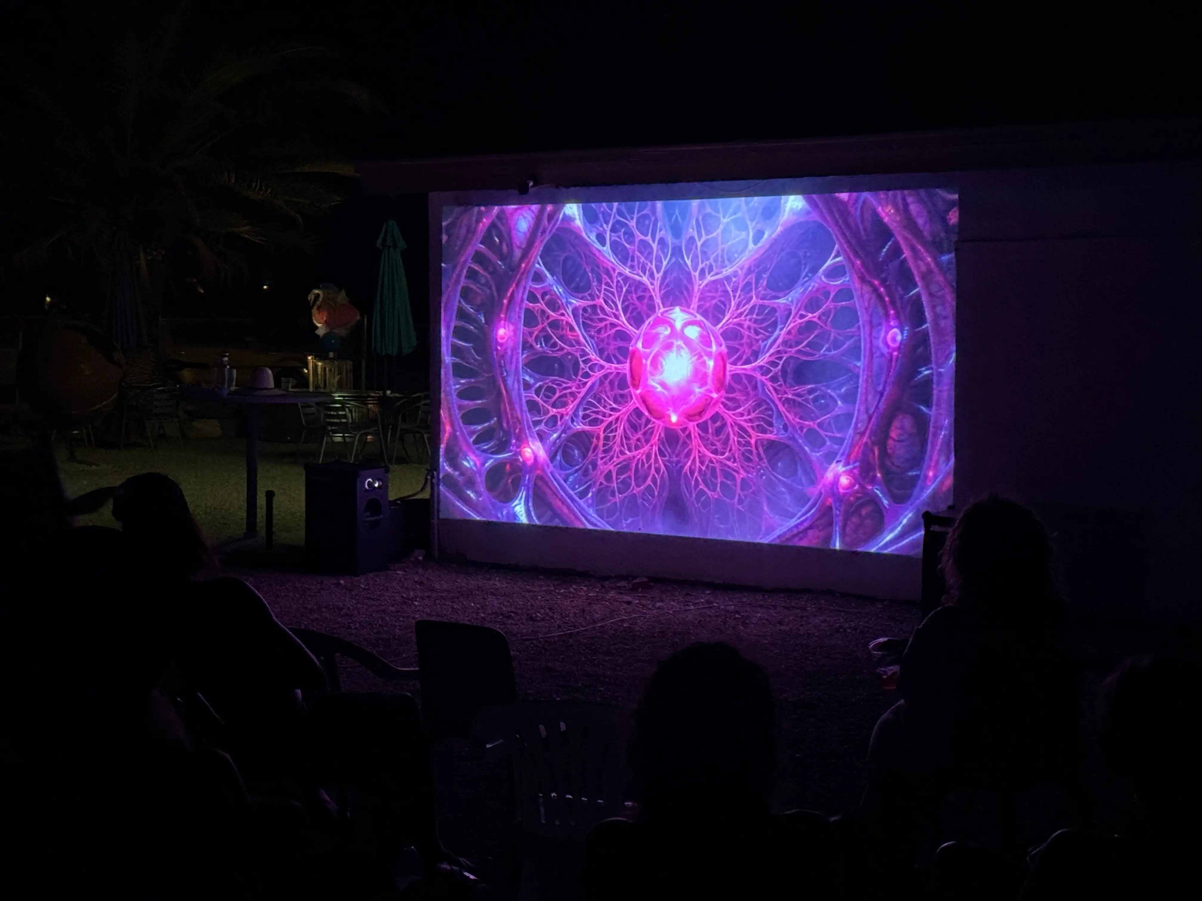 A generative fractal film glowing over silhouetted viewers · 2026