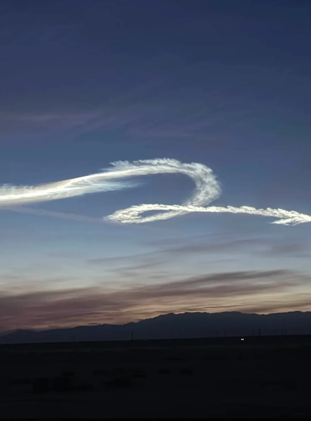 A rocket contrail swirl over the desert at dusk
