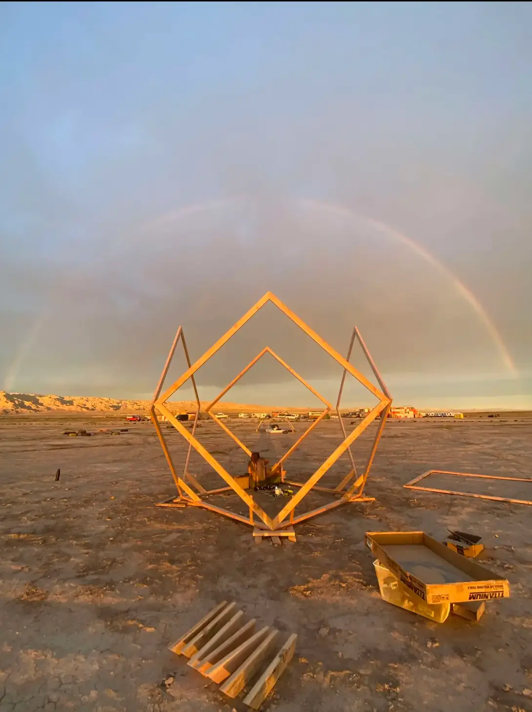 A geometric wooden sculpture beneath a desert rainbow