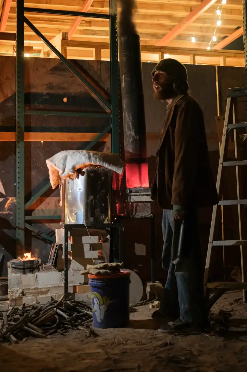 Standing beside a glowing kiln inside the workshop at night