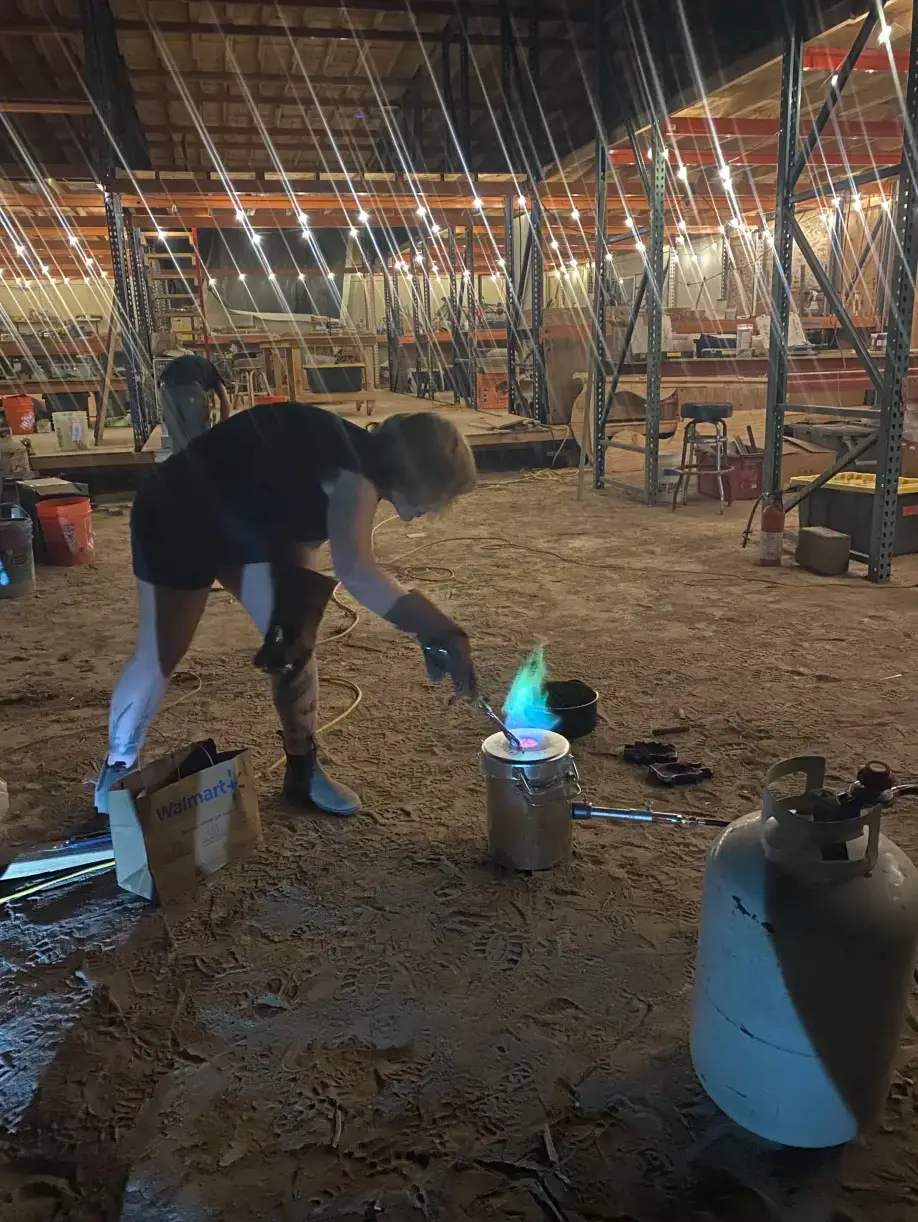 A blue flame rising from a small furnace on the workshop floor