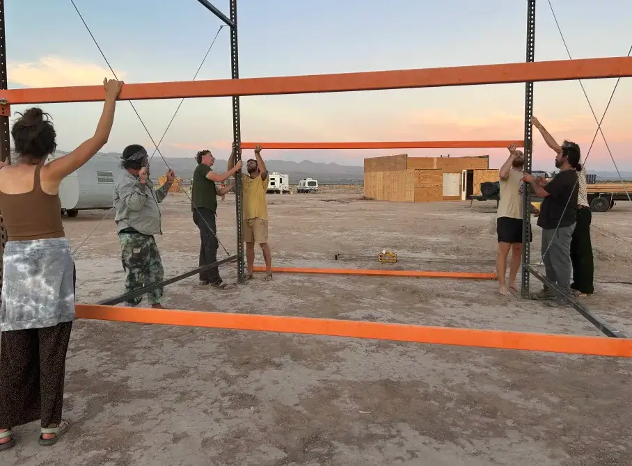 Residents raising the pallet-rack workshop frame at dusk