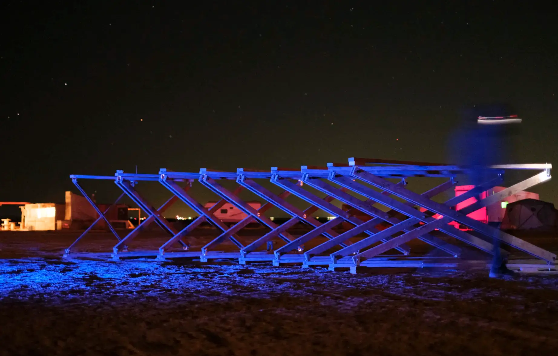 A deployable structure lit blue and pink against the night