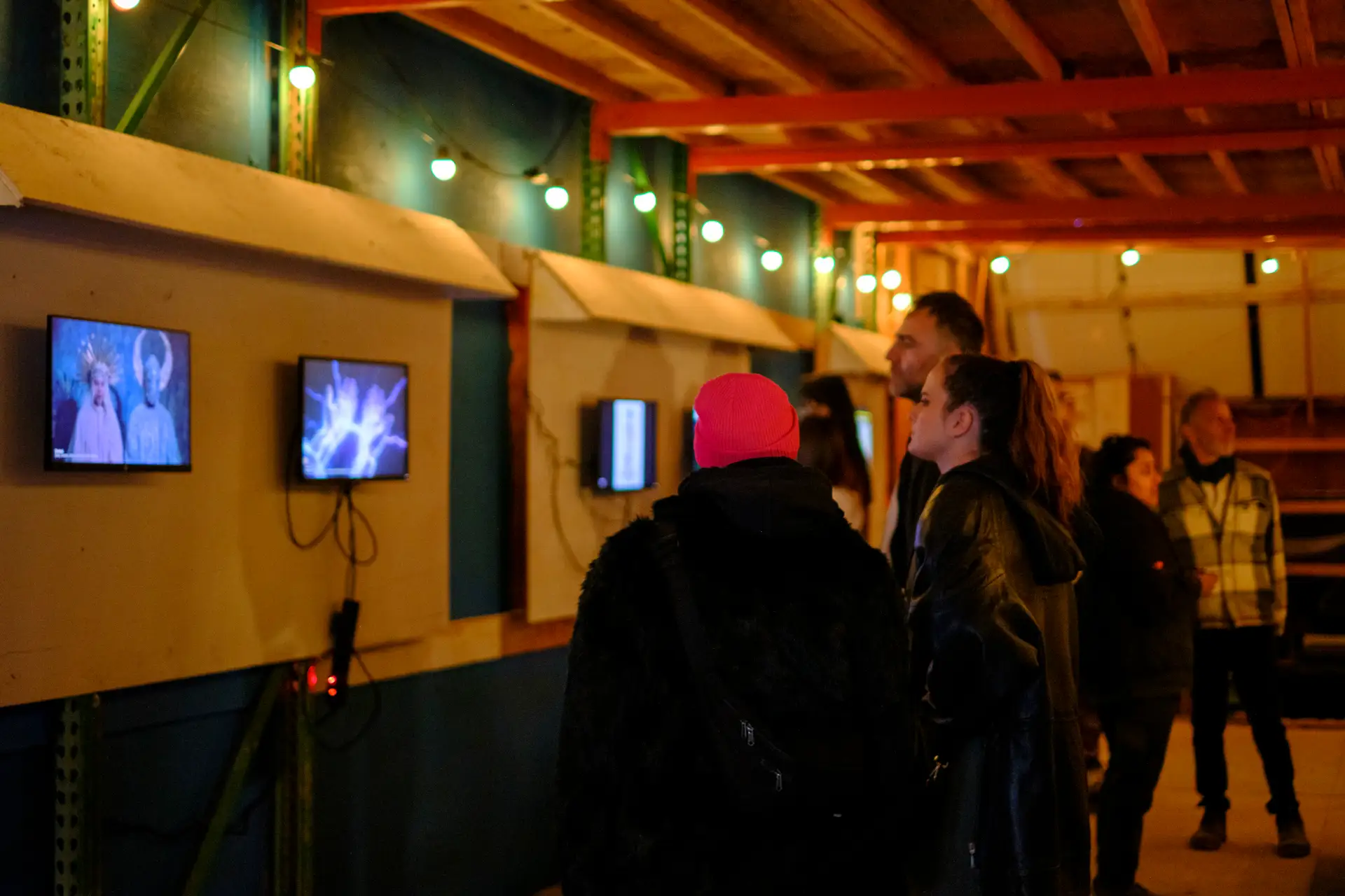 Visitors viewing video works on wall-mounted screens at the Chiba gallery opening, Mars 2026